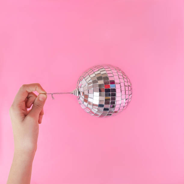 istock A hand with big shiny silver disco bauble hanging horizontally against pink background. Minimal surreal concept for season greetings concpet or banner or card. Design for conceptual magazine editorial. Copy space 1447791876