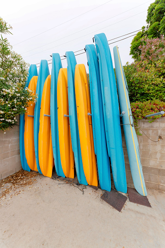Kayak boats on a rack near the concrete walls at Oceanside, California. Standing boats against the concrete walls with shrubs and plants on top.