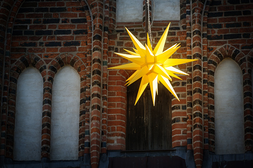 Yellow Moravian star hanging in front of an historic building in Luebeck, Germany, traditional street decoration for Advent, Christmas, and Epiphany, copy space, selected focus