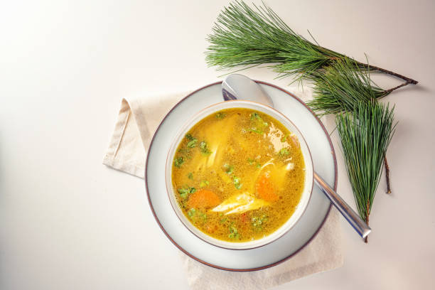 Healthy curry soup with chicken, vegetables and parsley in a bowl, home remedy against cold and flu in autumn and winter, light table with pine branches, copy space, top view from above stock photo