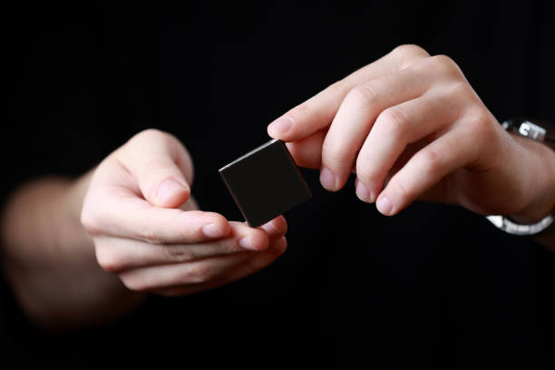 istock Mans hands holding a square little black box with an copy empty space for text and design isolated on dark background. Board, blank, template, mockup, layout for a slogan or inscription. 1447796772