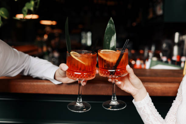 mani di donna e uomo tintinnano, applausi con bicchieri di cocktail spritz. coppia che celebra il matrimonio, anniversario con cocktail spritz, con arancia e verdure bevanda alcolica rinfrescante - bancone bar foto e immagini stock