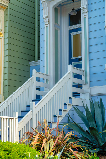 Blue timber house facade with white accent paint on stairs and gaurd rails with a front door background. On modern house in the neighborhood or in suburban part of the city downtown with row of homes