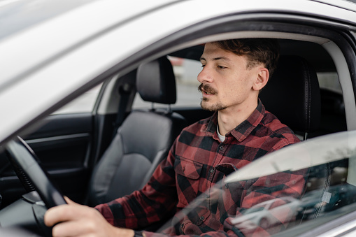 one man caucasian male with brown hair and mustaches sitting in a car adult driver wear shirt while driving automobile travel transport concept real people copy space