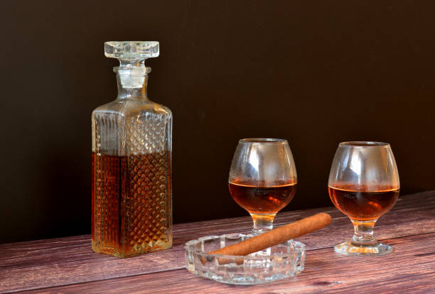 charuto cubano em um cinzeiro, dois copos e um decanter de cristal com uísque em uma mesa de madeira. - decanter crystal carafe glass - fotografias e filmes do acervo