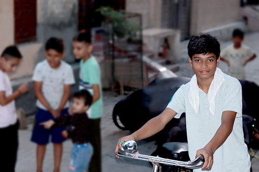 Teenage boy of Indian ethnicity standing with cycle and some of street children standing behind him.