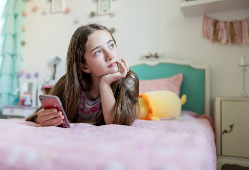 Thoughtful teenage girl at home using her cell phone and looking away - lifestyle concepts