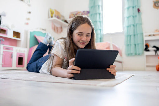 Happy teenage girl in her bedroom looking at social media app on her tablet computer - lifestyle concepts