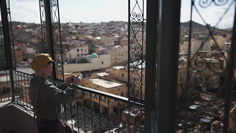 Asian Chinese female tourist photographing at rooftop Chouwara Leather traditional tannery in ancient medina of Fes El Bali, Morocco, Africa.