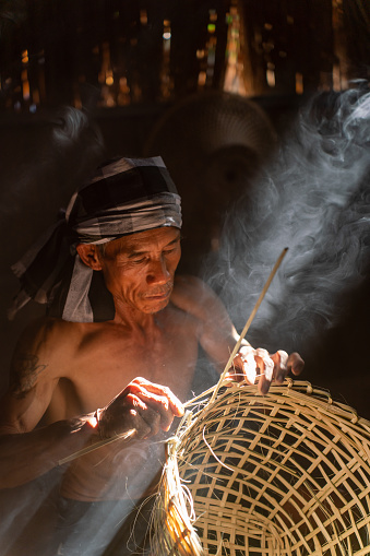 Asian village lifestyle, moment a local male adult uncle basket weaver maker making bamboo basket and hat in a dry grass built room, very beautiful scenic view