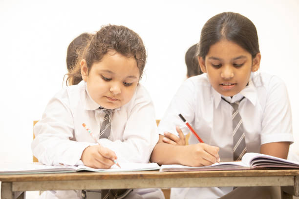 istock Indian elementary school students sitting at desk in classroom with writing in notebook with pencil, Examination and test, Girl Education concept. 1447832578