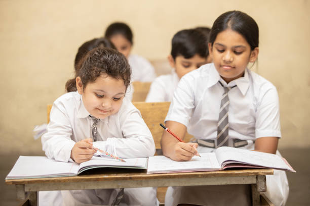 istock Indian elementary school girl students sitting at desk in classroom 
 writing in textbook. 1447832586