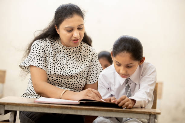 istock Indian mature teacher helping a student in elementary school lessons in classroom. female child studying in classroom, Girl Education concept. 1447832601