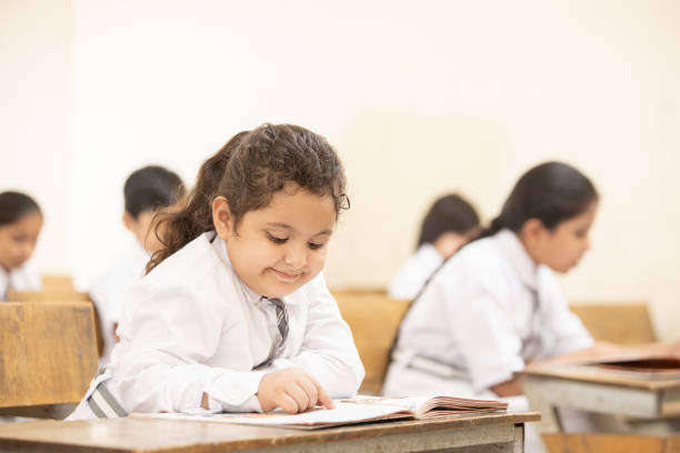 Indian elementary school students sitting at desk  studying in classroom reading notebook, Girl Education concept.