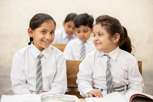 Happy Indian elementary schoolgirls students sitting at desk in classroom with writing in notebook with pencil, Examination and test, female Education concept.