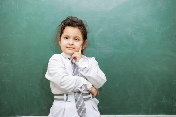 Smart little Indian school girl kid thinking expression standing against blank chalkboard or blackboard. Education concept. copy space.