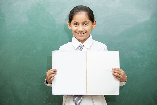 Portrait of happy indian school girl student showing blank notebook, female education concept, copy space.