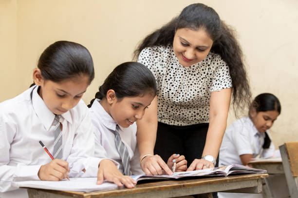 istock Indian mature teacher helping a student in elementary school lessons in classroom. female child studying in classroom, Girl Education concept. 1447834010