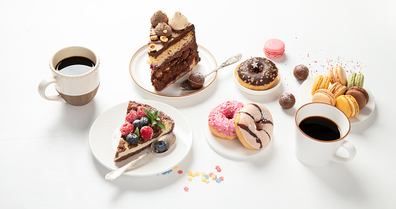 Table with various cookies, donuts, cakes, cheesecakes and coffee cups on white background.  Delicious dessert table.