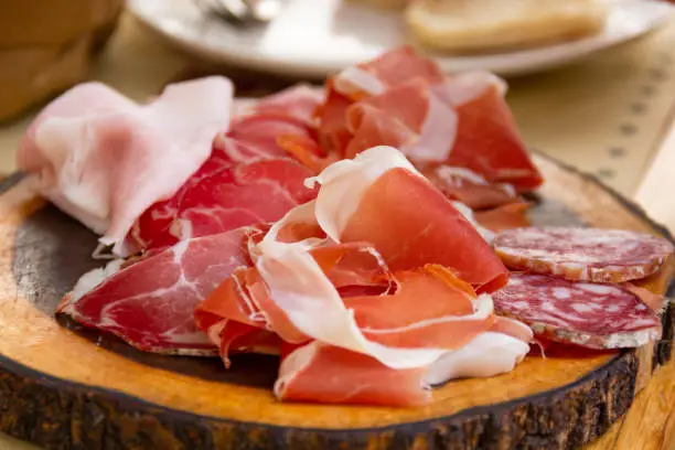 Traditional Spanish tapas of smoked ham, salami and prosciutto on wooden board. Pork meat assortment, non vegetarian food concept
