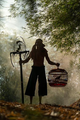 Asian village lifestyle, portrait of an adult male bird trainer and keeper in a forest near his house in Northeast Thailand.