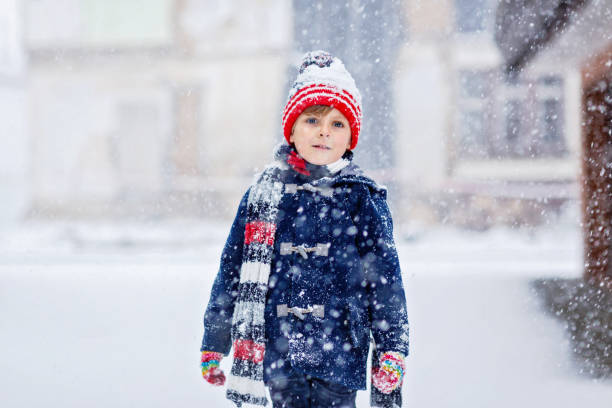 istock Funny little kid boy in colorful clothes playing outdoors during strong snowfall 1447841811
