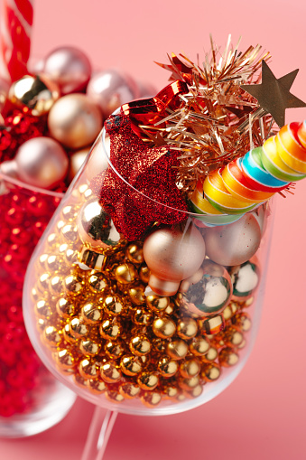 Glass with Christmas decorations on pink pastel background close up