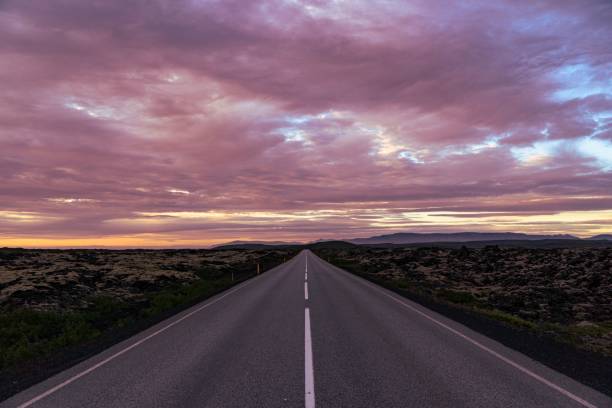 istock Beautiful pink sunset over an empty asphalt road surrounded by a green landscape 1447859773