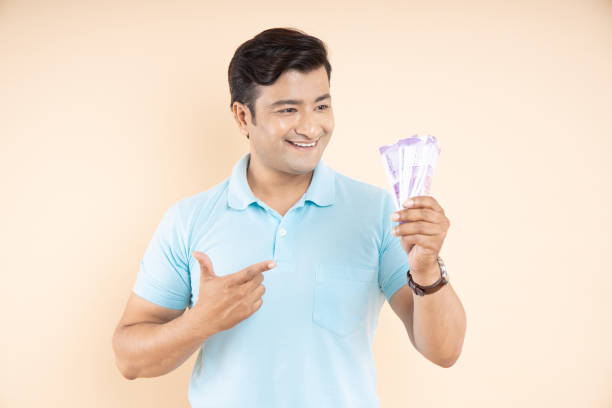 istock Portrait of happy Indian man pointing at rupee notes isolated on beige studio background. Money saving and investing concept. 1447860229