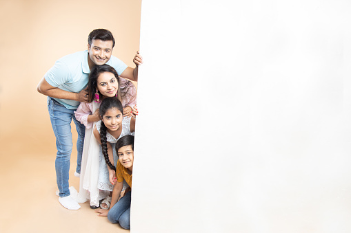 Advertising. Portrait of happy indian family with big big white empty banner or poster billboard for content, place for text or image isolated on plane studio background