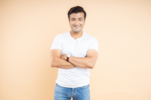 Smiling Handsome young indian man wearing white casual t-shirt and jeans isolated on beige studio background.
