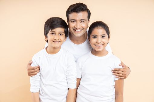 Happy young indian father with his two kids wearing white casual t-shirt standing over isolated beige background.