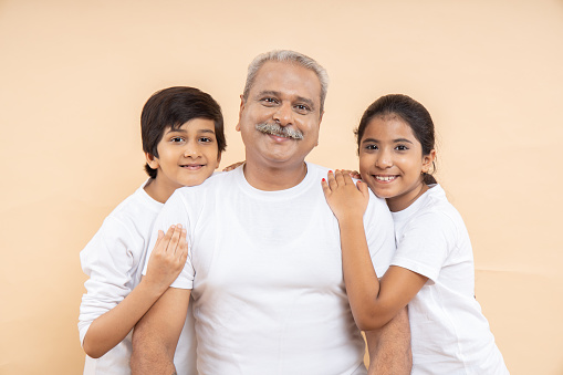 Happy indian senior man with kids wearing white casual t-shirt standing over isolated beige background.
