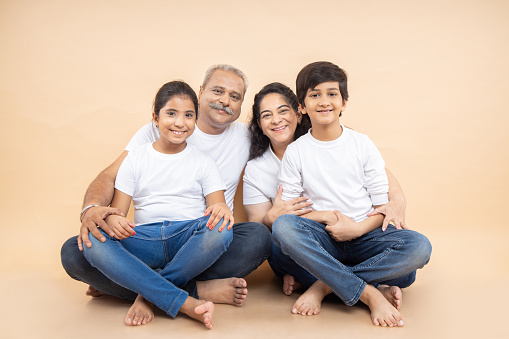 Happy indian grandparents with kids wearing white casual t-shirt sitting together over isolated beige background.