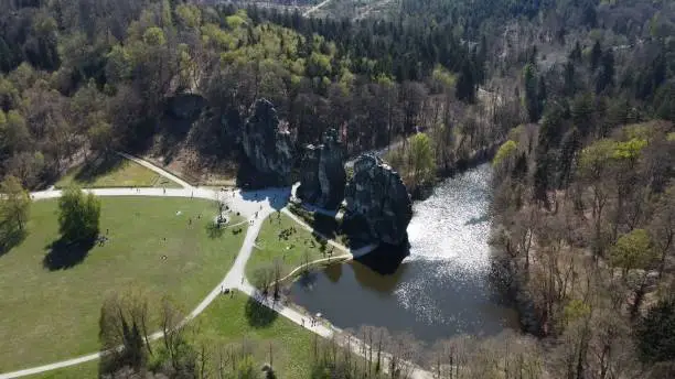 An aerial view of the Externsteine sandstone rock formation surrounded by greenery and a river on the right side