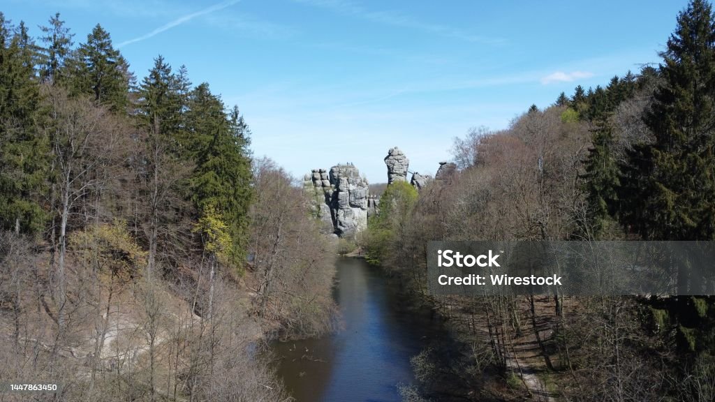 View of a river surrounded by dry trees with the Externsteine in the background A view of a river surrounded by mostly dry trees with the Externsteine sandstone rock formation in the background Awe Stock Photo