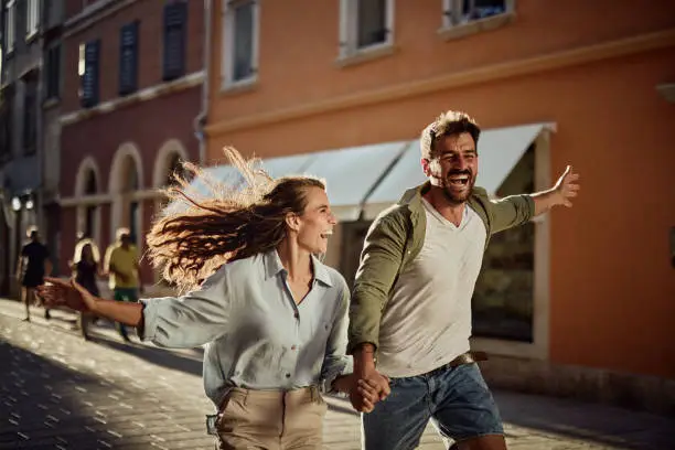Photo of Joyful couple running on the city street.