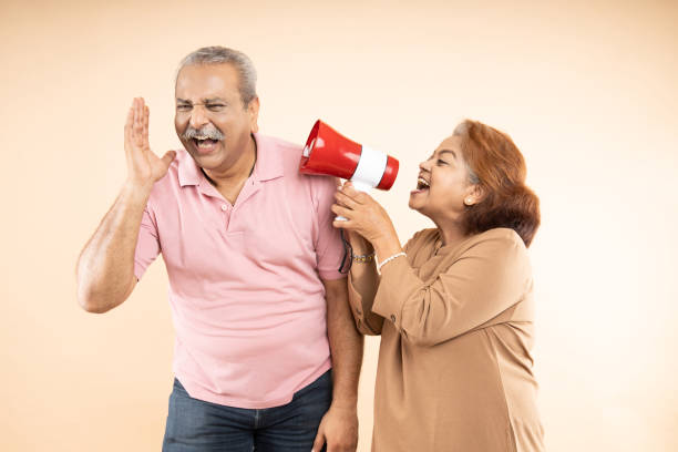 Senior indian woman scream or shouting at man in megaphone isolated on beige background. announce discounts sale. Asian wife tease husband. Senior indian woman scream or shouting at man in megaphone isolated on beige background. announce discounts sale. Asian wife tease husband. divorce india stock pictures, royalty-free photos & images