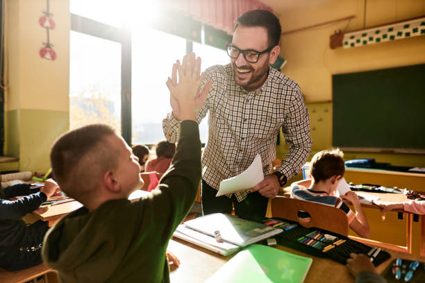 istock Happy male teacher giving high-five to his elementary student on a class in the classroom. 1447868472
