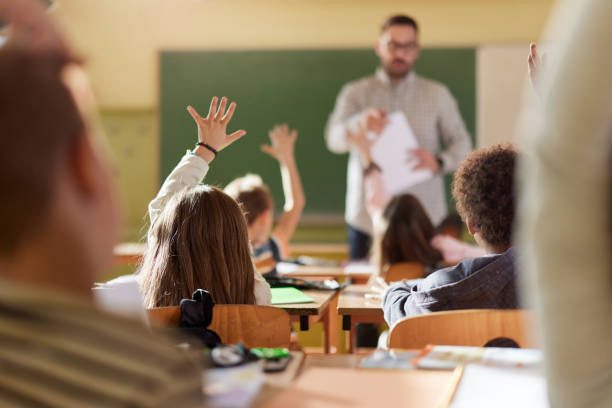 istock Back view of students raising their hands to answer the teacher's question on a class. 1447868512