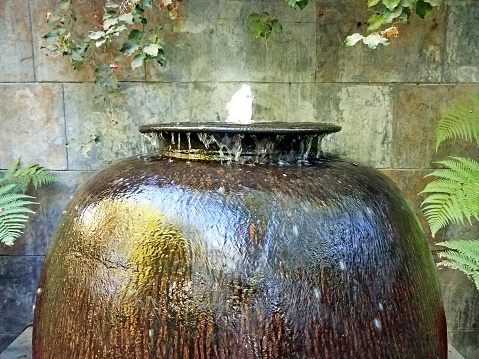 Glistening reflective brown pot with bubbling fountain in front of a wall