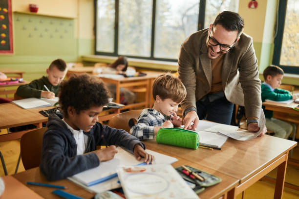 istock Young happy professor assisting his elementary students on a class at school. 1447868673