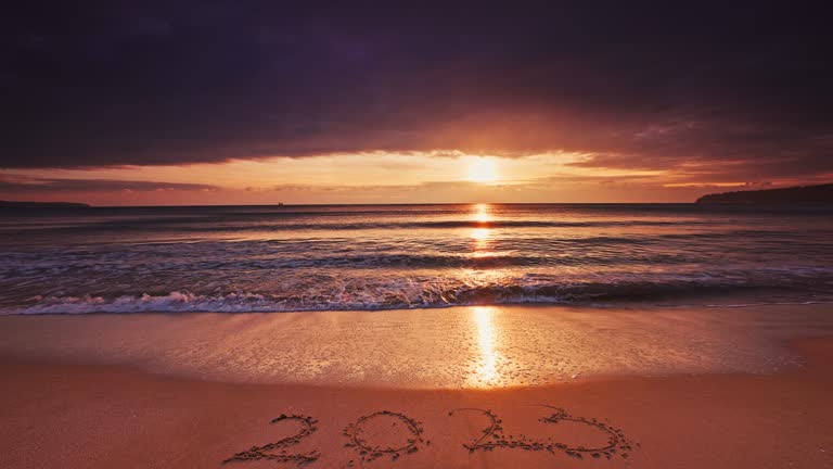 2023 Welcome new year text on the sea shore during ocean sunrise. Beach sunset and waves washing the sand, 4k video with Sound