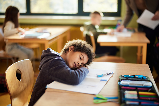 Tired black schoolboy fell asleep on a class at elementary school.