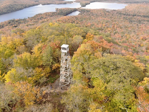 Aerial of Kane Mountain Fire Tower with autumn forest scape water near Fulton County, New York