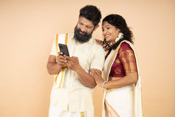 istock Happy South indian couple using mobile phone isolated on beige background. 1447871492