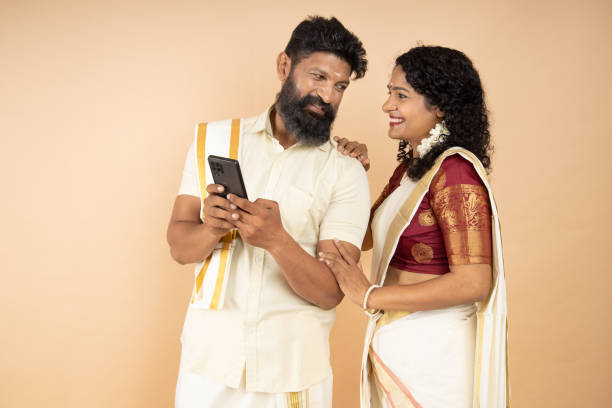 istock Happy South indian couple using mobile phone isolated on beige background. 1447871542