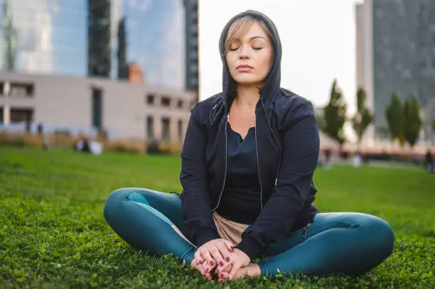 Photo of Zen like in the city, young curvy  woman taking a break after workout meditating in a public park