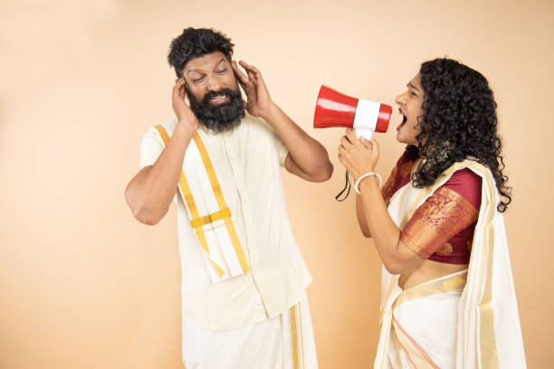 South indian woman scream or shouting at man in megaphone to tease him isolated on beige background. announce discounts sale. South indian woman scream or shouting at man in megaphone to tease him isolated on beige background. announce discounts sale. divorce india stock pictures, royalty-free photos & images