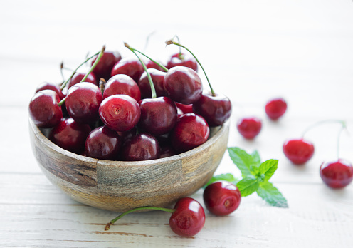 Fresh red cherries fruit in bowl on a white wooden background